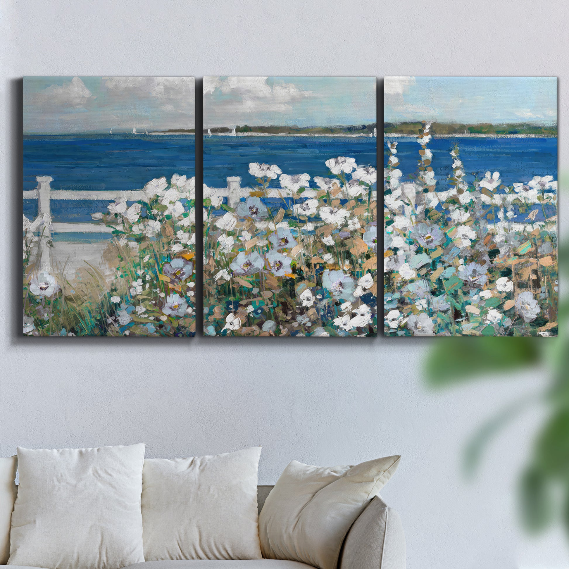 Three-panel canvas wall art featuring coastal garden overlooking bay, displayed in a living room above a sofa.