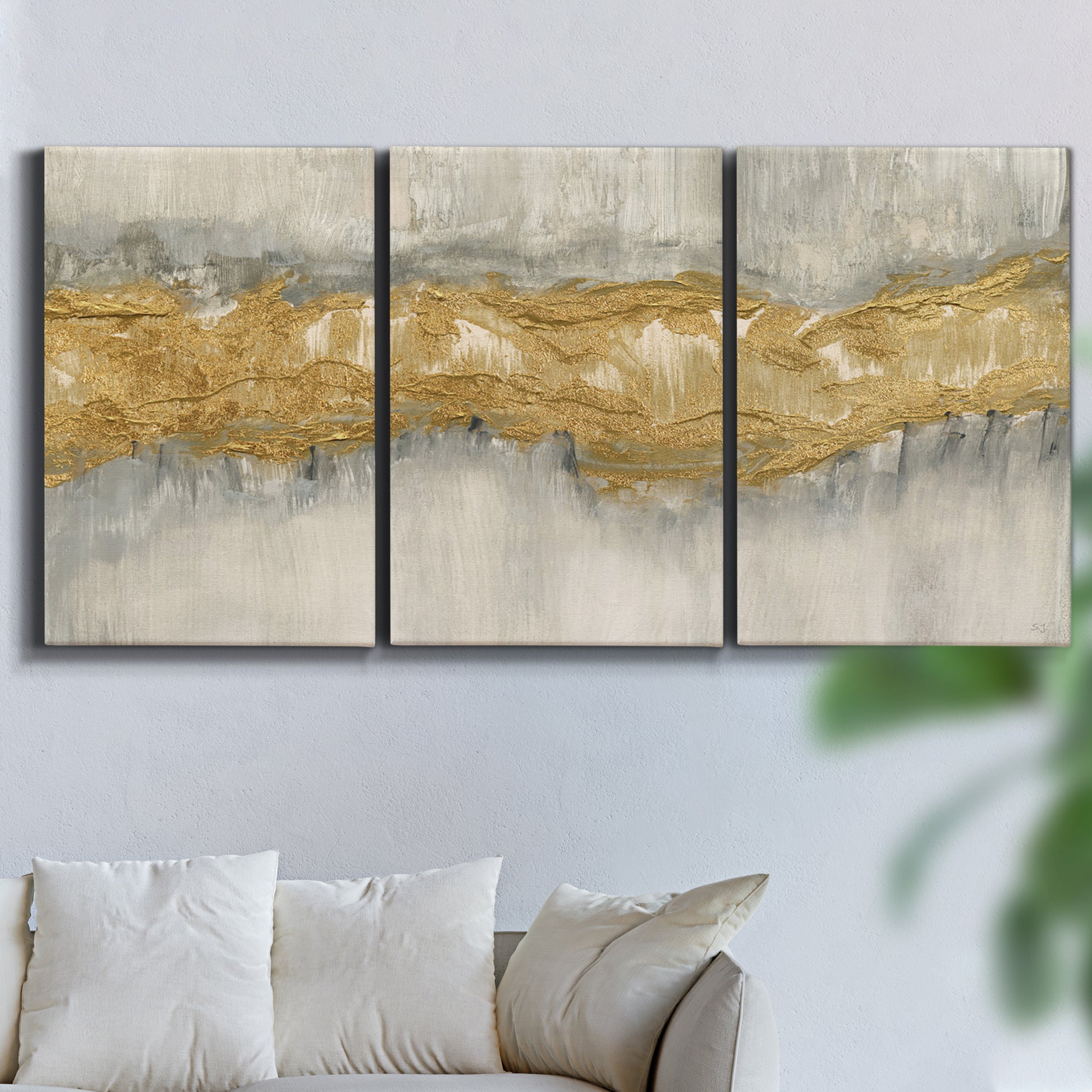 Three-panel canvas wall art featuring flowing abstract golden tones, displayed in a living room above a sofa.