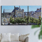 Three-panel canvas wall art featuring gothic church within city setting, displayed in a living room above a sofa.