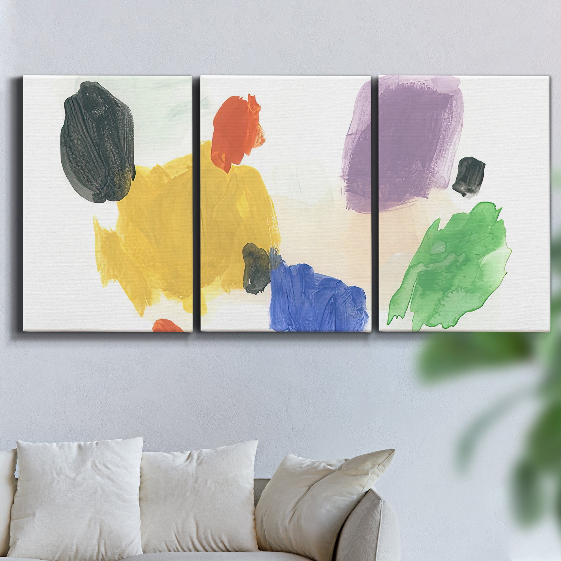 Three-panel canvas wall art featuring inkblot style abstract color symmetry, displayed in a living room above a sofa.