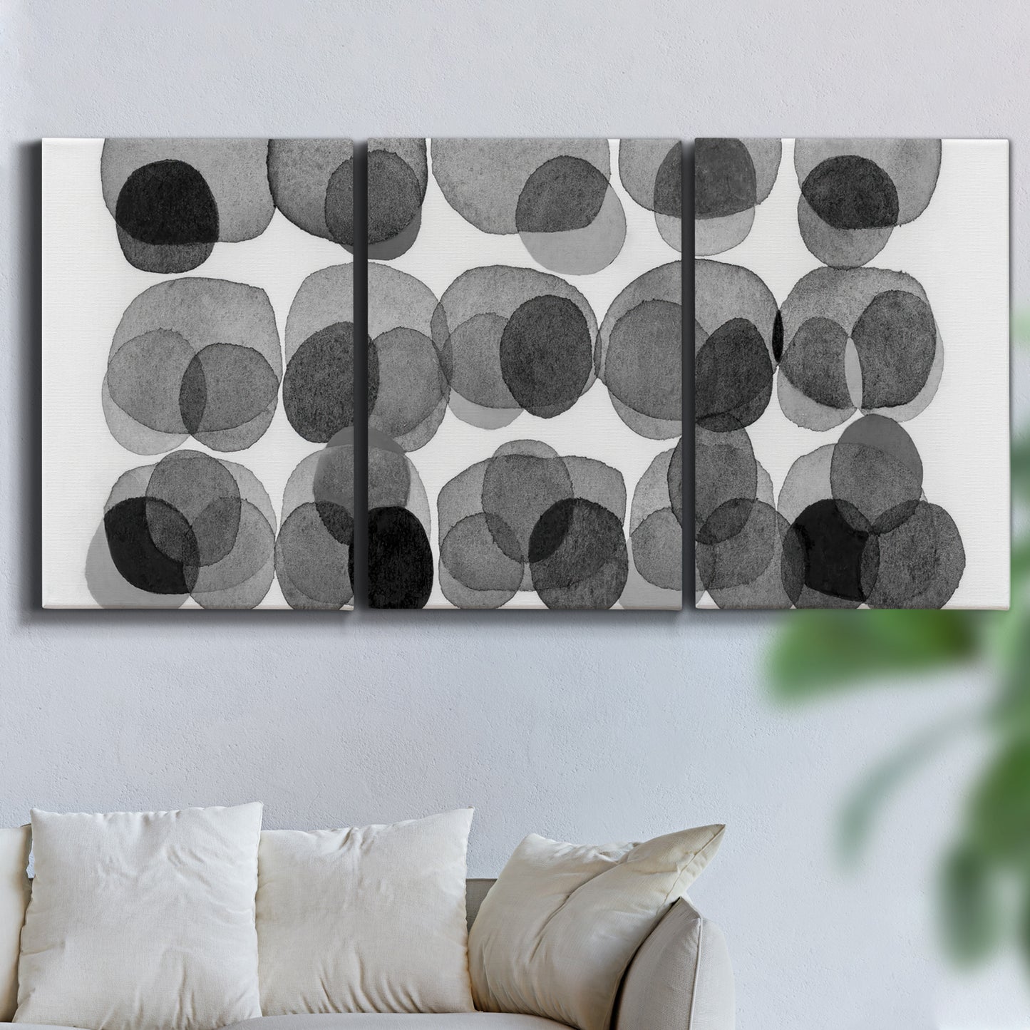 Three-panel canvas wall art featuring geometric abstract watercolor forms, displayed in a living room above a sofa.