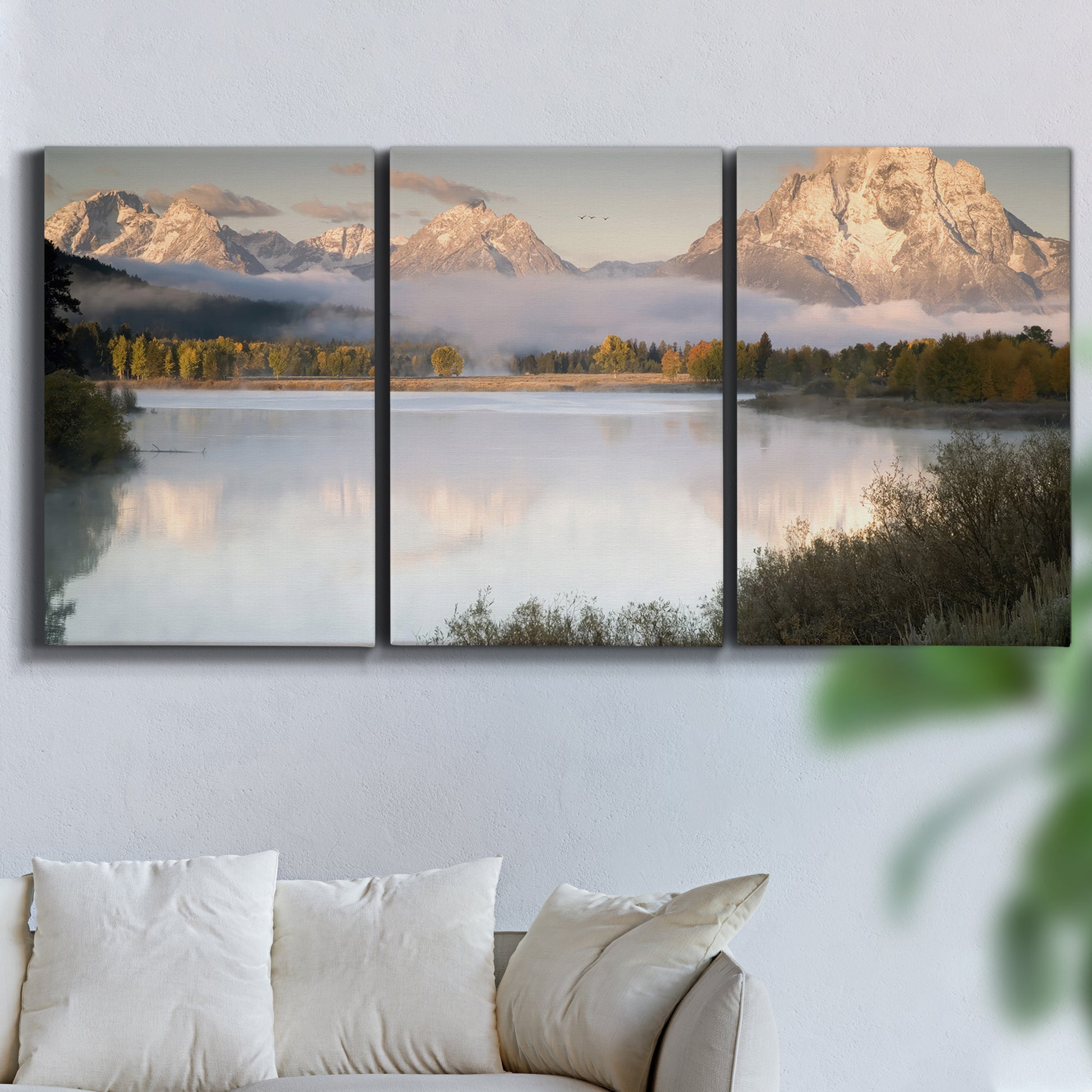 Three-panel canvas wall art featuring fog drifting over winding river, displayed in a living room above a sofa.