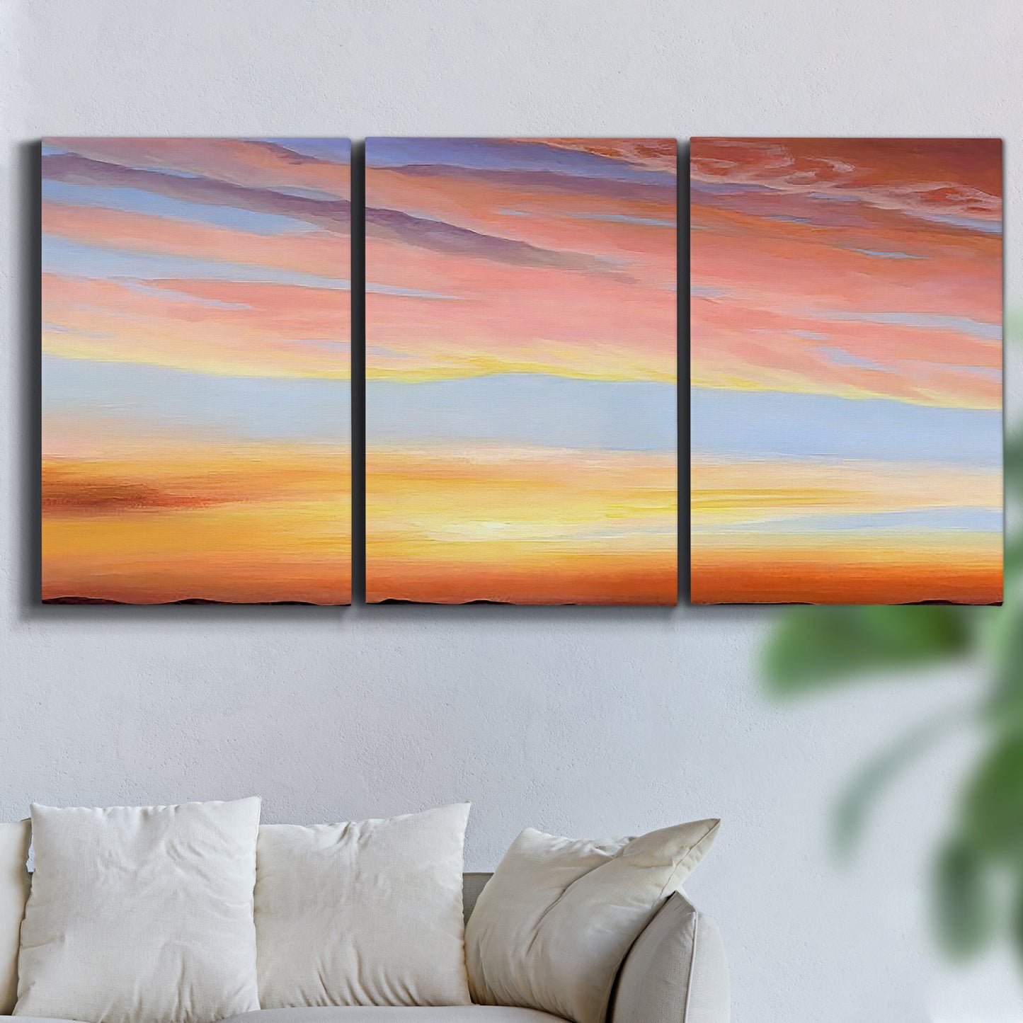 Three-panel canvas wall art featuring glowing sunset sky over landscape, displayed in a living room above a sofa.