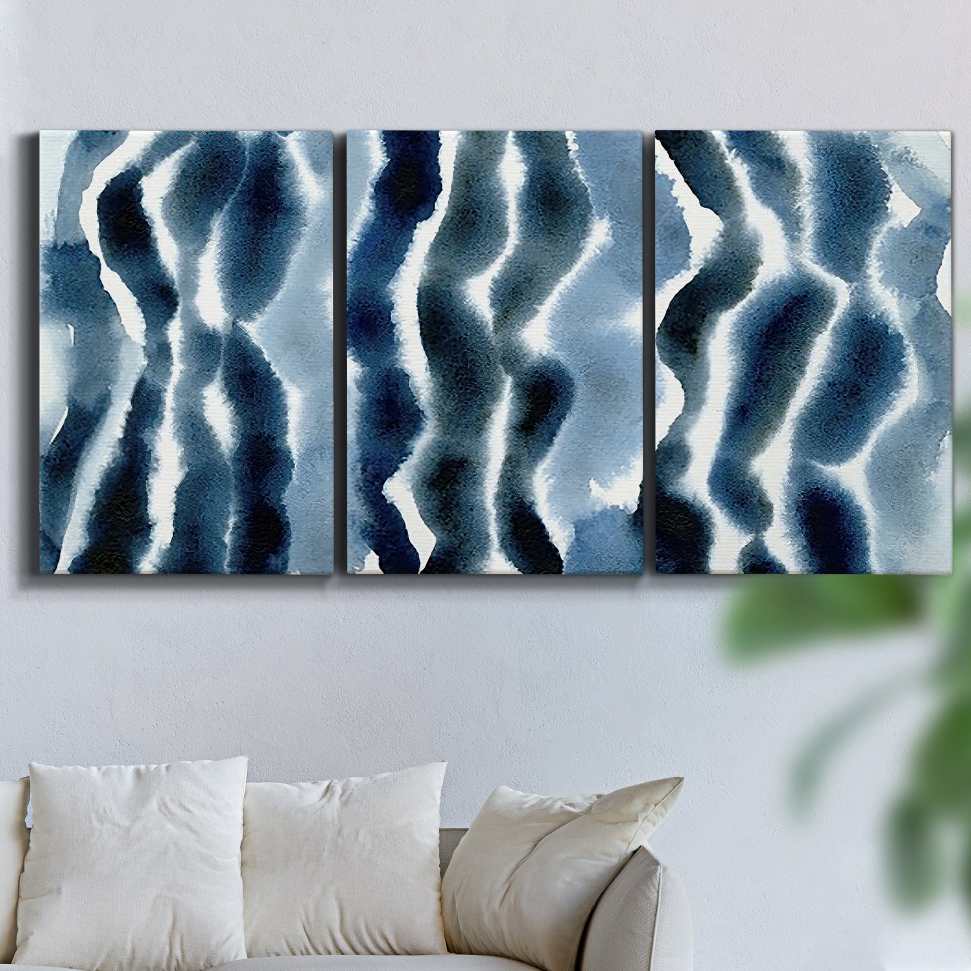 Three-panel canvas wall art featuring flowing blue watercolor wave forms, displayed in a living room above a sofa.