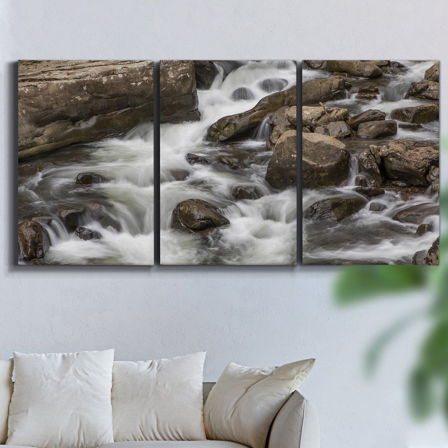 Three-panel canvas wall art featuring rushing river water over rocks, displayed in a living room above a sofa.