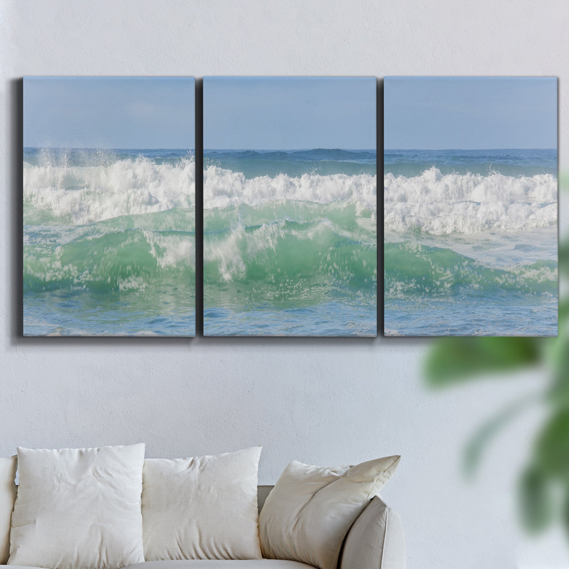 Three-panel canvas wall art featuring coastal waves breaking ashore, displayed in a living room above a sofa.