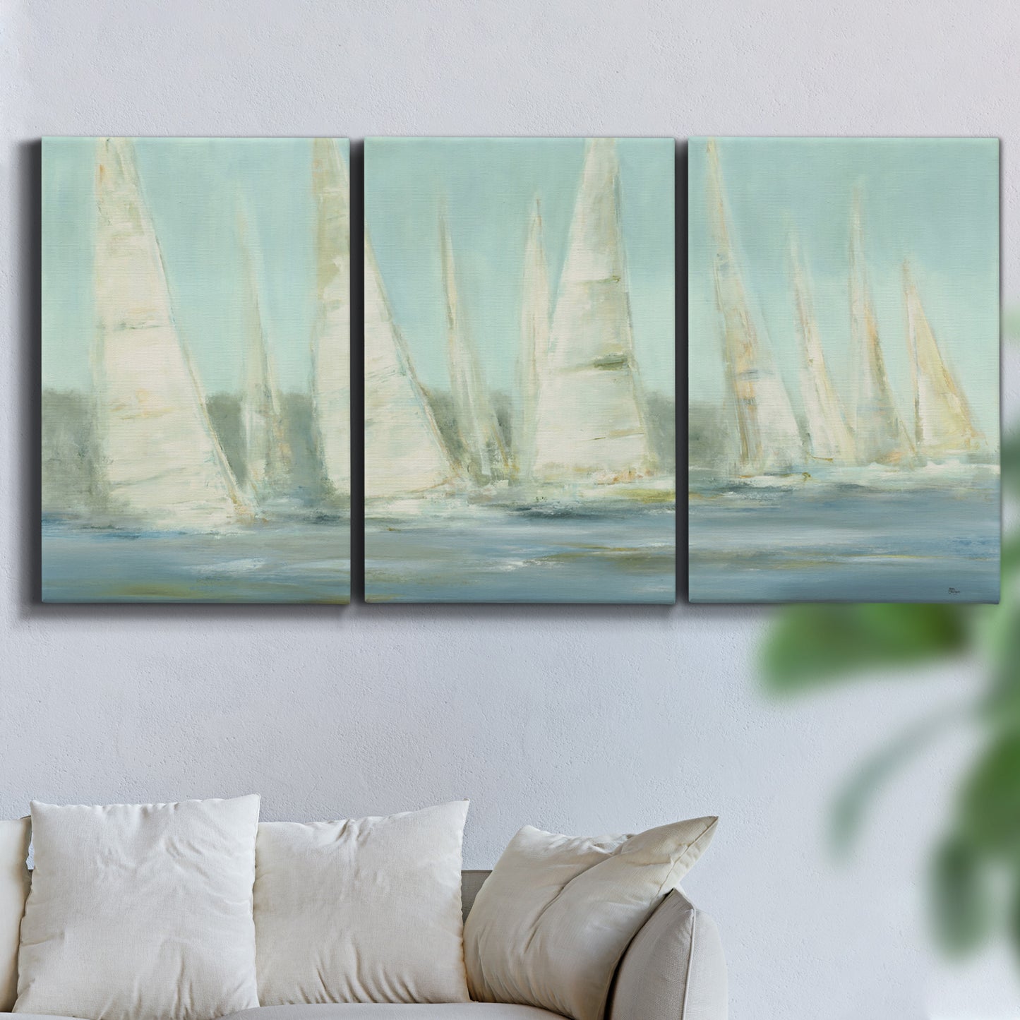 Three-panel canvas wall art featuring sailboats silhouetted at sunrise, displayed in a living room above a sofa.