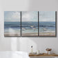 Three-panel canvas wall art featuring shore birds searching along beach, displayed in a bathroom above a bathtub.