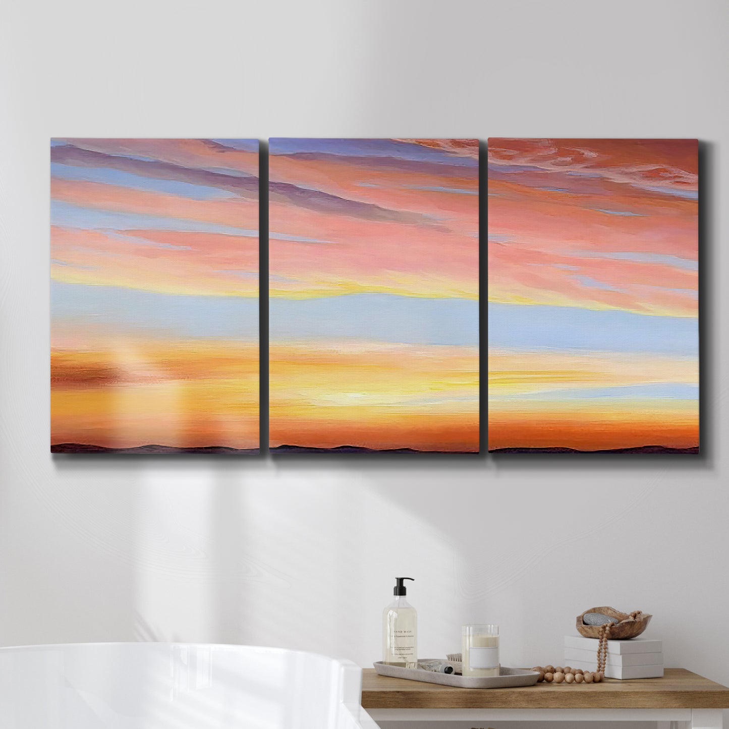 Three-panel canvas wall art featuring glowing sunset sky over landscape, displayed in a bathroom above a bathtub.