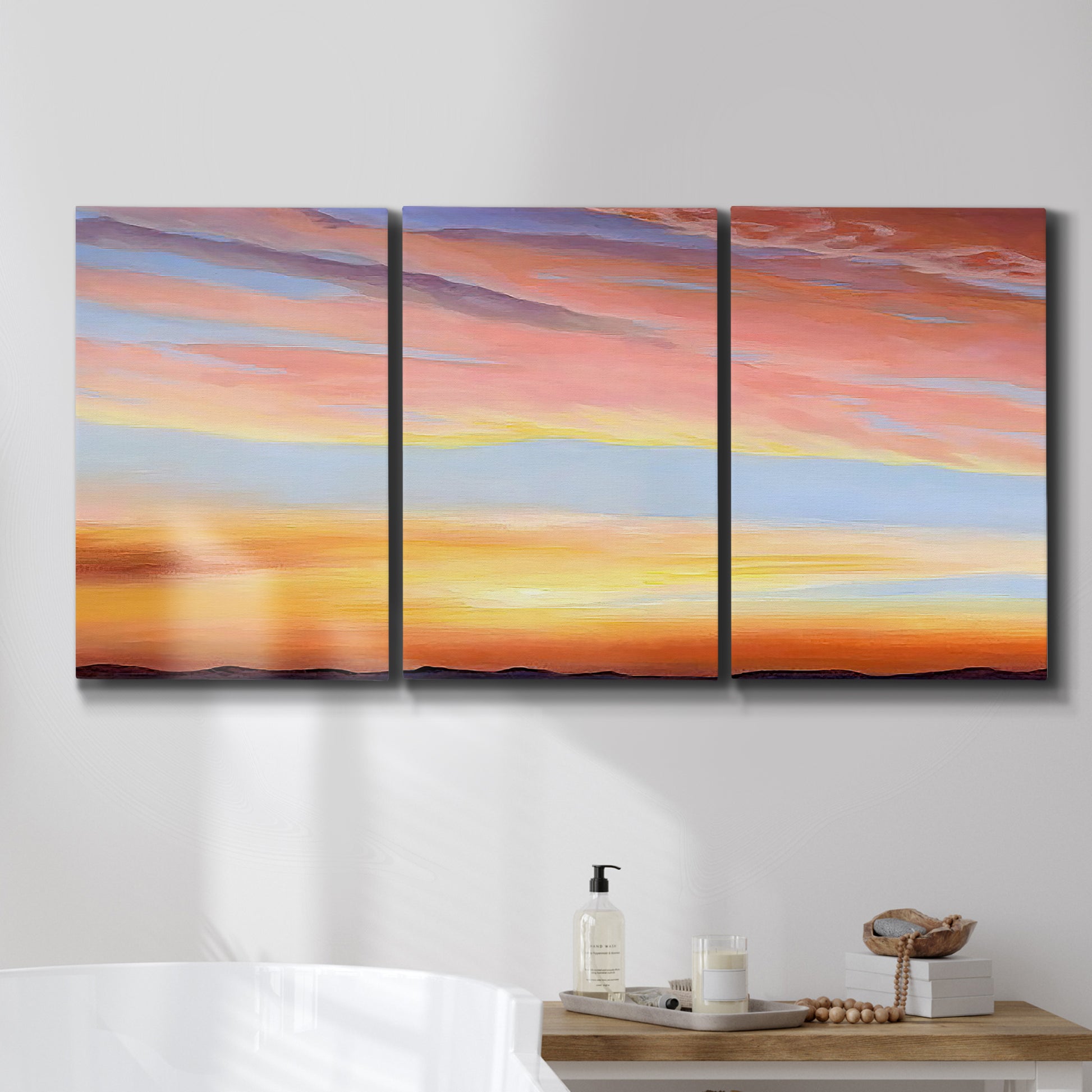 Three-panel canvas wall art featuring glowing sunset sky over landscape, displayed in a bathroom above a bathtub.