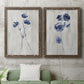 Set of two walnut barnwood framed canvas prints depicting a coordinated art pair of blue wildflower stems on weathered neutral paper rendered as rustic monochrome botanical paintings above a sofa in a modern living room.