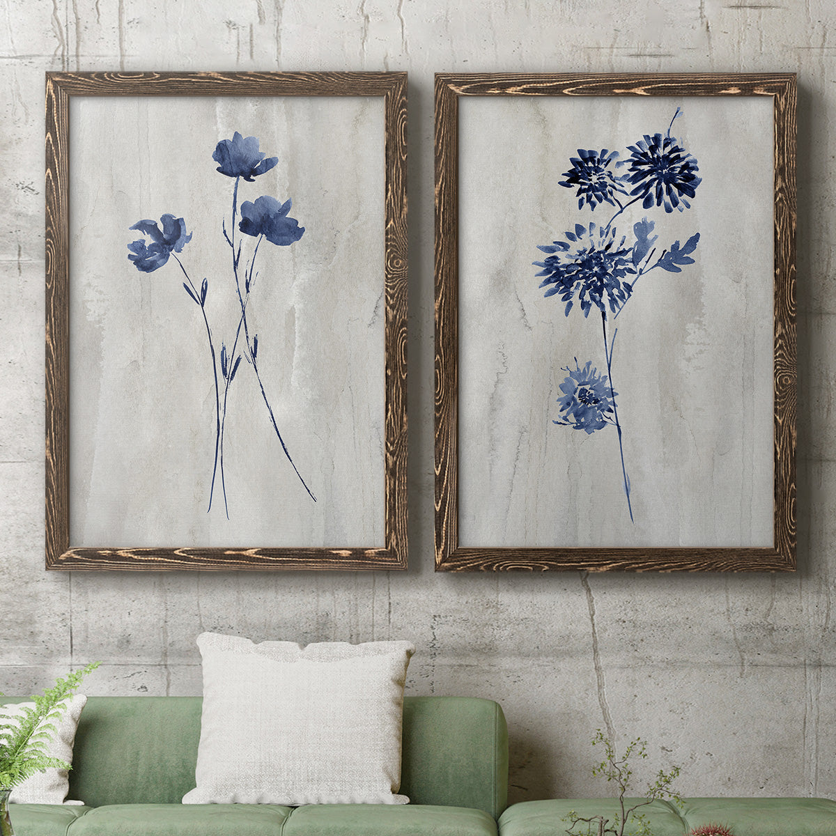 Set of two walnut barnwood framed canvas prints depicting a coordinated art pair of blue wildflower stems on weathered neutral paper rendered as rustic monochrome botanical paintings above a sofa in a modern living room.