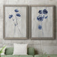 Set of two gray barnwood framed canvas prints depicting a coordinated art pair of blue wildflower stems on weathered neutral paper rendered as rustic monochrome botanical paintings above a sofa in a modern living room.