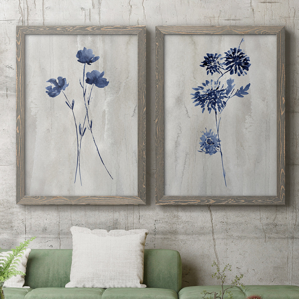 Set of two gray barnwood framed canvas prints depicting a coordinated art pair of blue wildflower stems on weathered neutral paper rendered as rustic monochrome botanical paintings above a sofa in a modern living room.