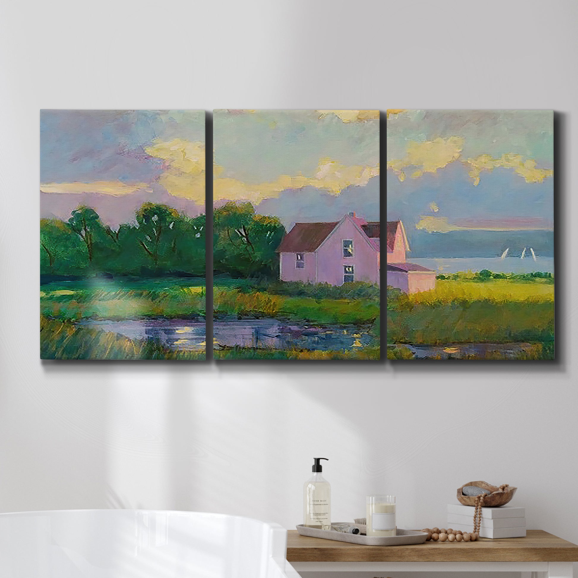 Three-panel canvas wall art featuring farmhouse near coastline landscape, displayed in a bathroom above a bathtub.