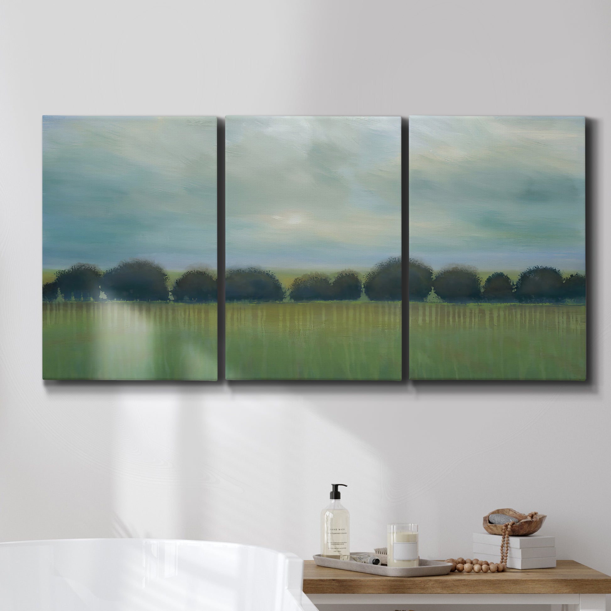 Three-panel canvas wall art featuring rolling green pastoral fields, displayed in a bathroom above a bathtub.