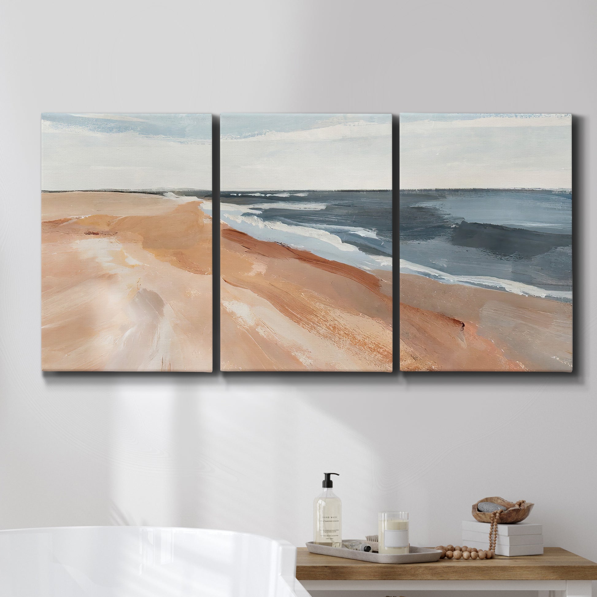Three-panel canvas wall art featuring abstract coastal beach composition, displayed in a bathroom above a bathtub.