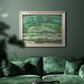 Impressionist garden scene with Japanese bridge and water lilies by Claude Monet in an ornate champagne frame displayed in a dark-toned interior setting.