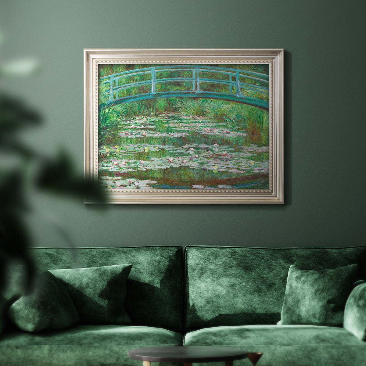 Impressionist garden scene with Japanese bridge and water lilies by Claude Monet in an ornate champagne frame displayed in a dark-toned interior setting.