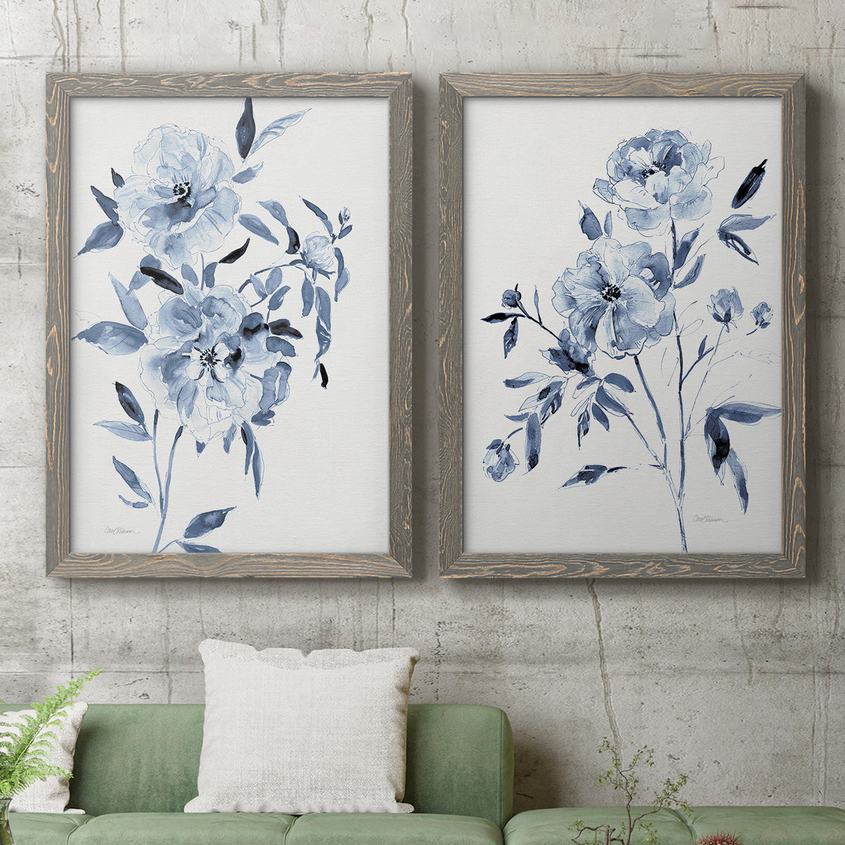 Set of two gray barnwood framed canvas prints depicting a coordinated art pair of loose blue flowers and leafy branches rendered as expressive watercolor botanical paintings above a sofa in a modern living room.