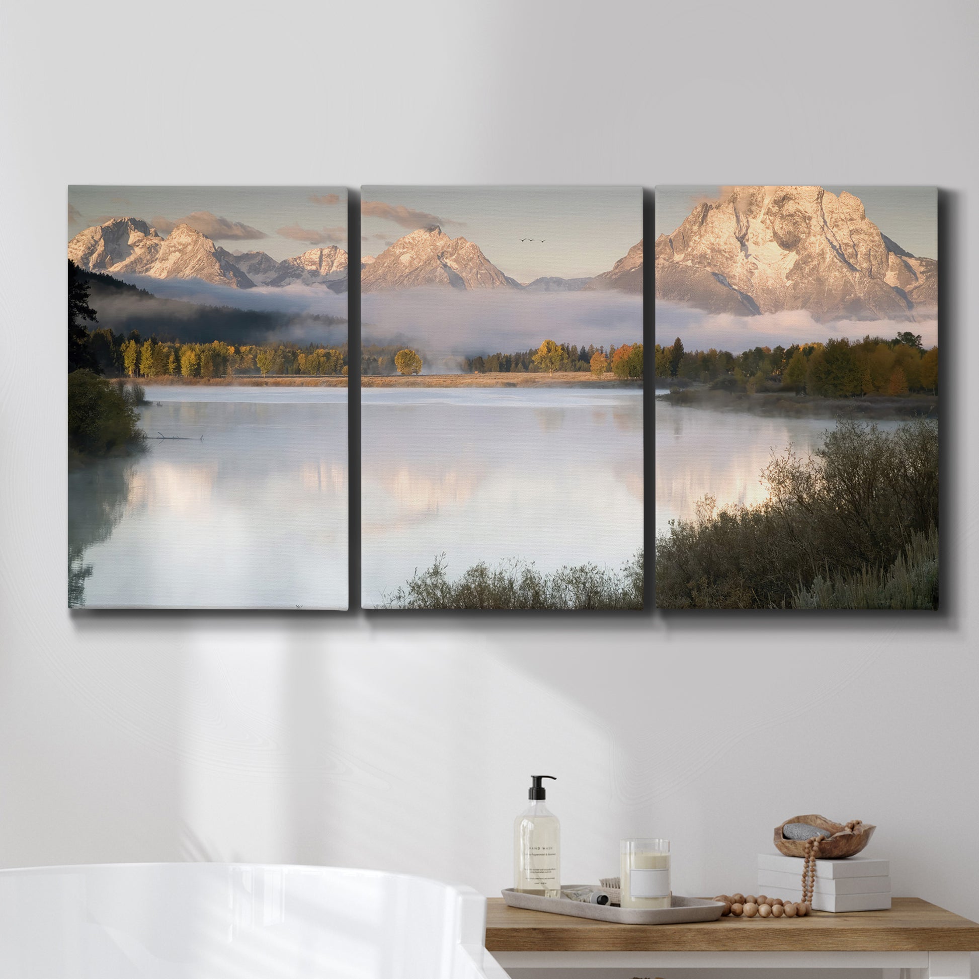 Three-panel canvas wall art featuring fog drifting over winding river, displayed in a bathroom above a bathtub.