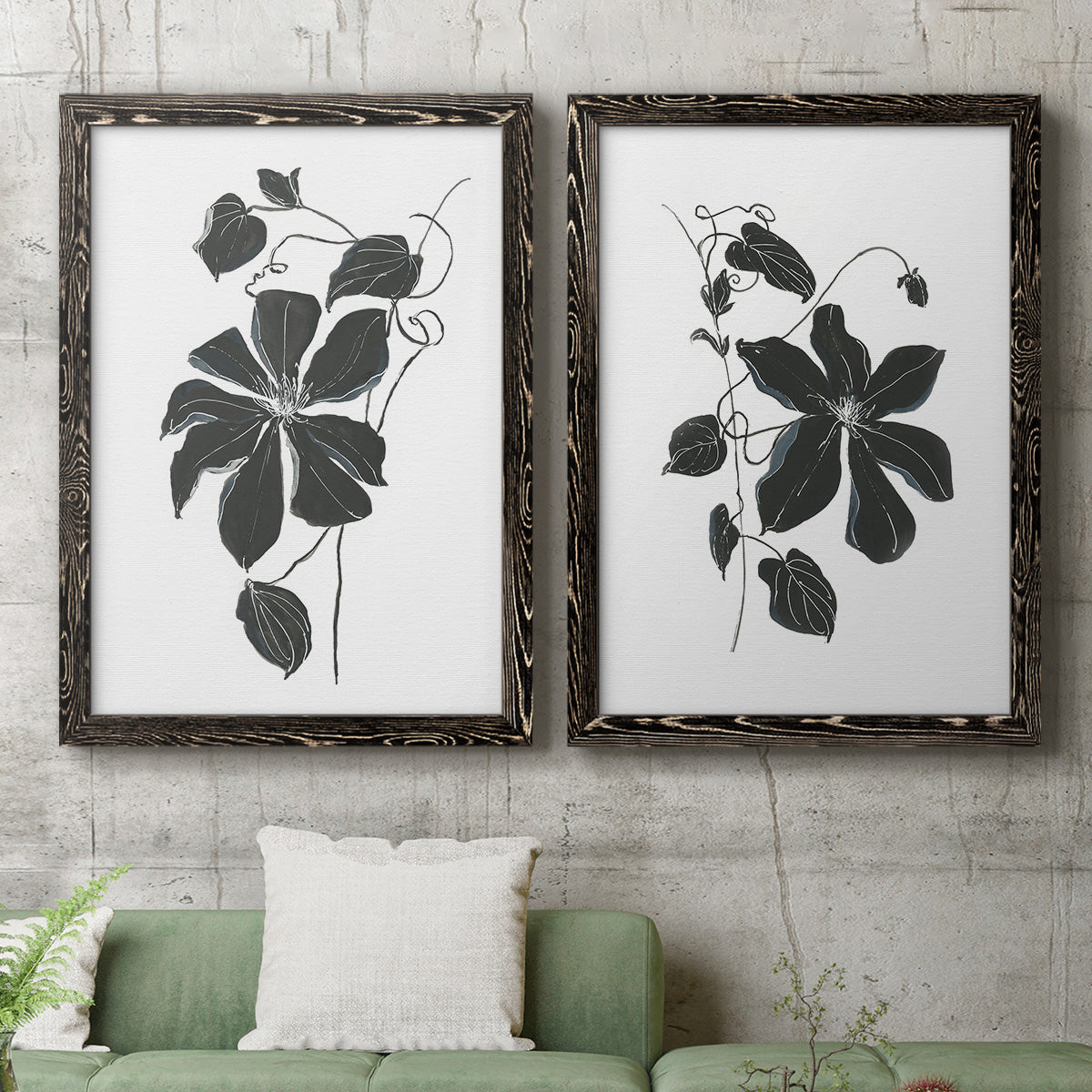 Set of two black barnwood framed canvas prints depicting a coordinated art pair of black leafy vine silhouettes rendered as minimalist botanical prints above a sofa in a modern living room.