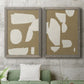 Set of two gray barnwood framed canvas prints depicting a coordinated art pair of irregular white cutout-like shapes on taupe grounds rendered as bold minimalist shape abstracts above a sofa in a modern living room.