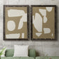 Set of two black barnwood framed canvas prints depicting a coordinated art pair of irregular white cutout-like shapes on taupe grounds rendered as bold minimalist shape abstracts above a sofa in a modern living room.