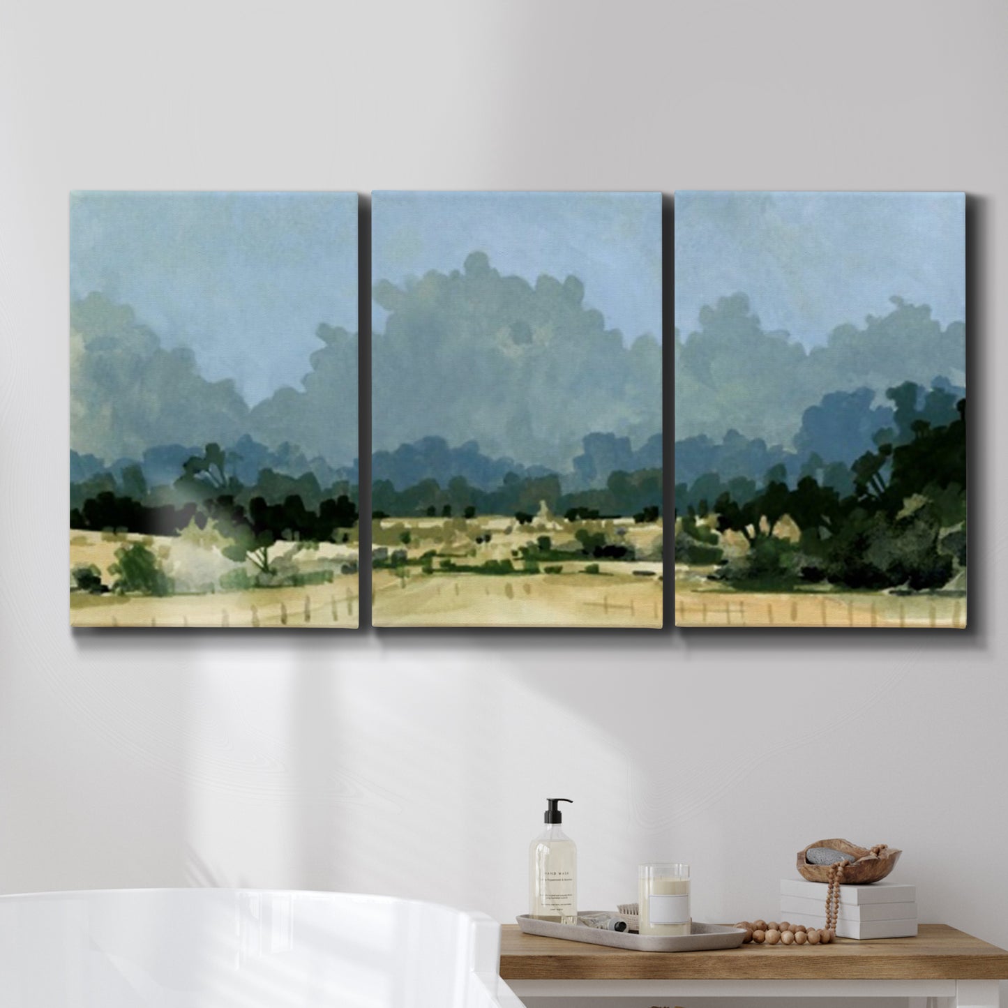 Three-panel canvas wall art featuring rural farmland landscape in watercolor, displayed in a bathroom above a bathtub.