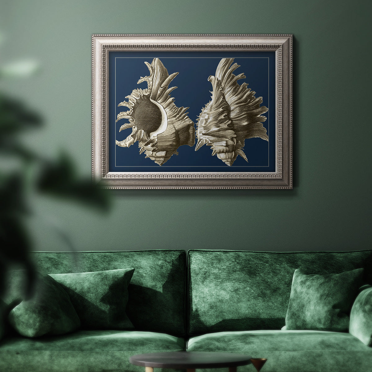 Vintage nautical conch shell artwork on navy background in an ornate vintage silver frame displayed in a dark-toned interior setting.