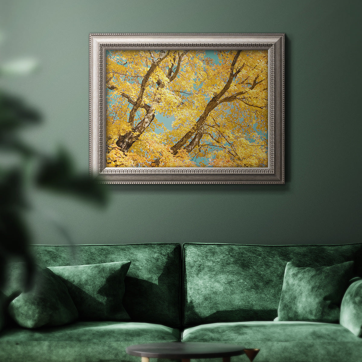 Vibrant yellow autumn leaves on branches in an ornate vintage silver frame displayed in a dark-toned interior setting.