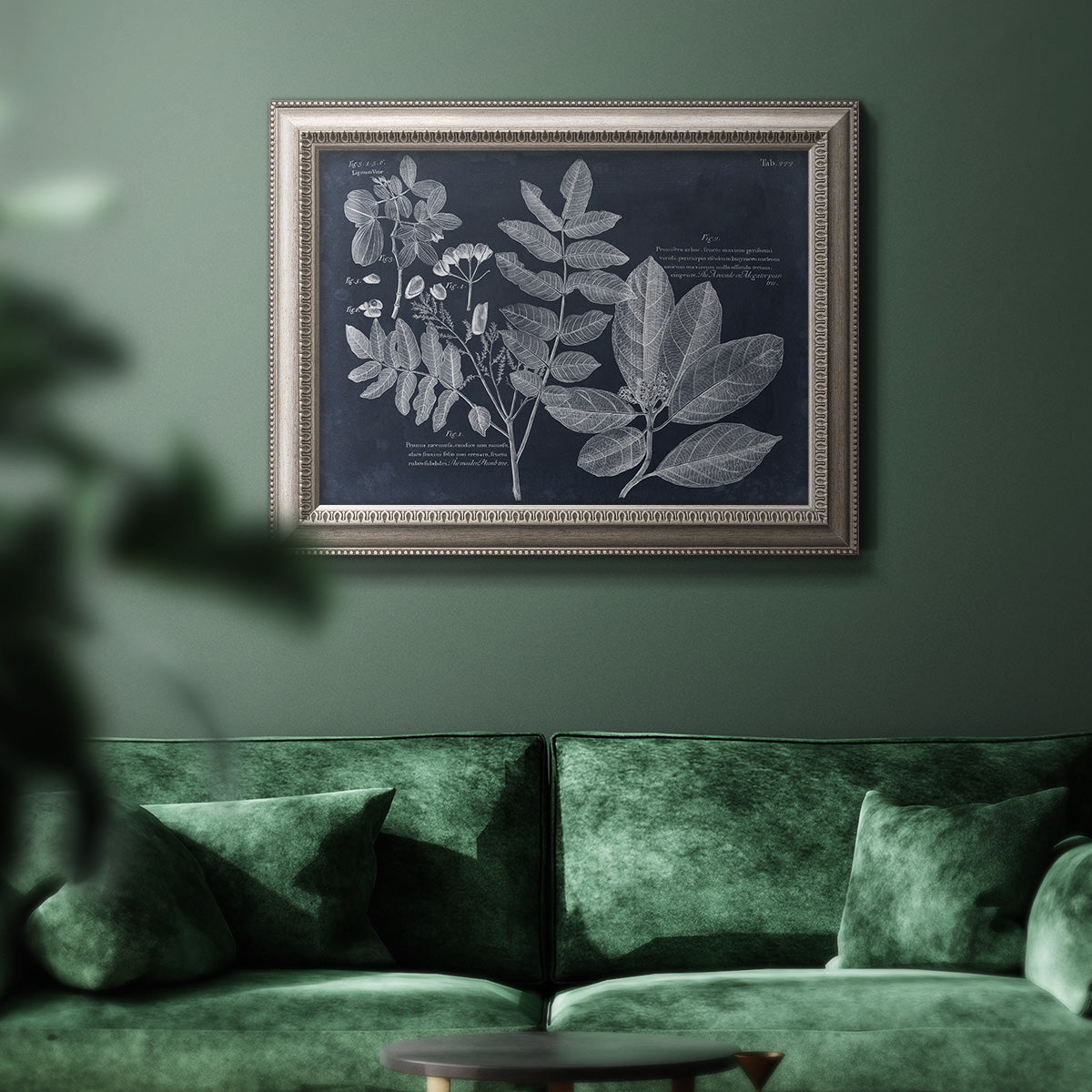 Antique botanical foliage artwork on navy background in an ornate vintage silver frame displayed in a dark-toned interior setting.