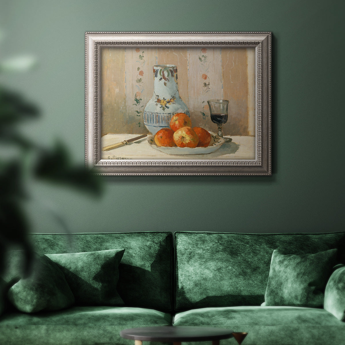 Impressionist still life painting with apples and a ceramic pitcher in an ornate vintage silver frame displayed in a dark-toned interior setting.