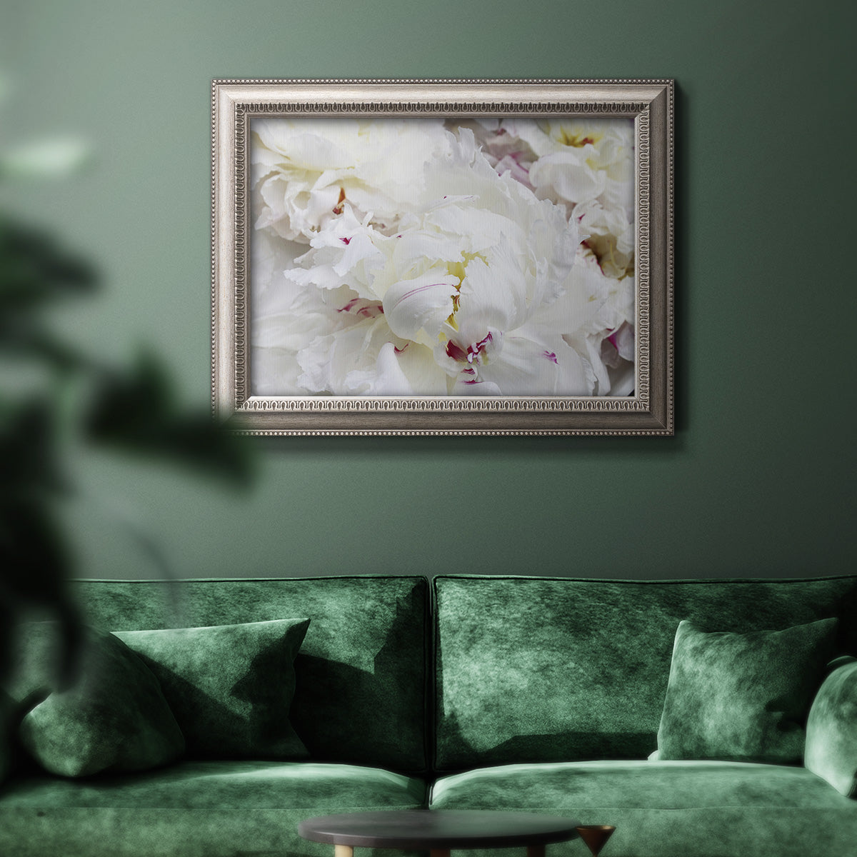White peonies in bloom in an ornate vintage silver frame displayed in a dark-toned interior setting.