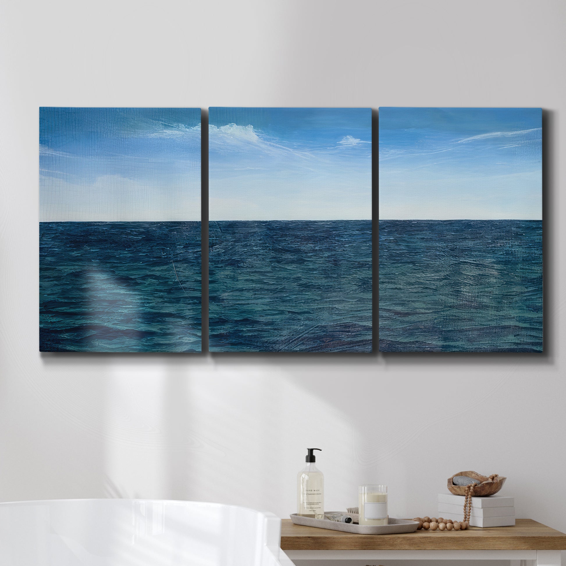 Three-panel canvas wall art featuring open water landscape with wide horizon, displayed in a bathroom above a bathtub.
