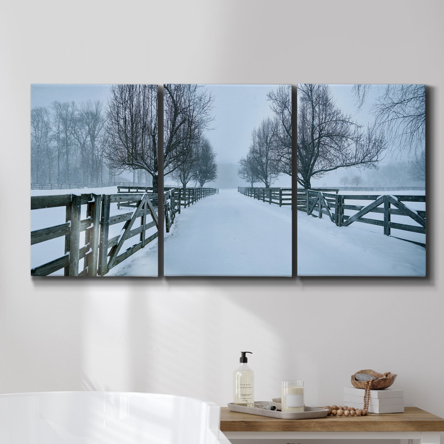 Three-panel canvas wall art featuring snow covered rural road photograph, displayed in a bathroom above a bathtub.
