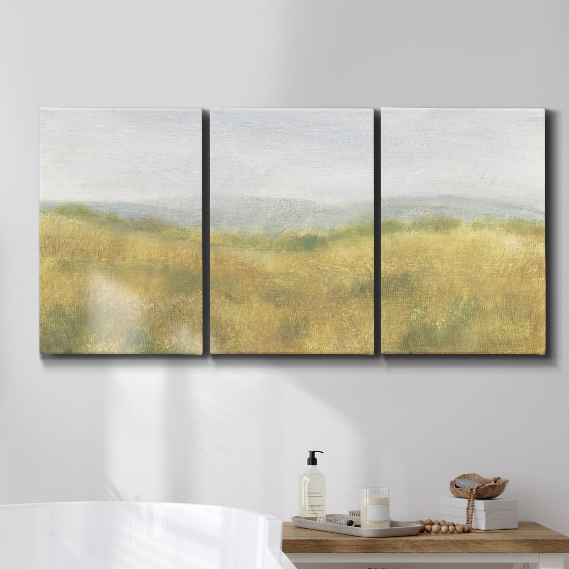 Three-panel canvas wall art featuring pastoral wheat field landscape, displayed in a bathroom above a bathtub.