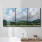 Three-panel canvas wall art featuring pastoral mountain landscape in blue, displayed in a bathroom above a bathtub.