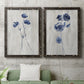 Set of two black barnwood framed canvas prints depicting a coordinated art pair of blue wildflower stems on weathered neutral paper rendered as rustic monochrome botanical paintings above a sofa in a modern living room.