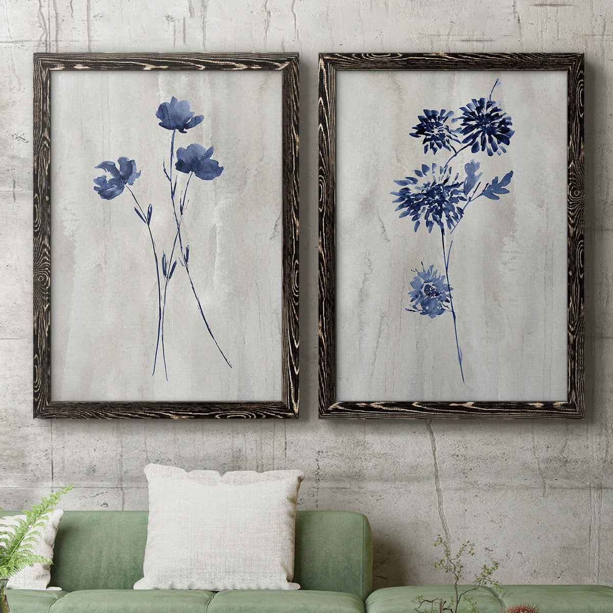 Set of two black barnwood framed canvas prints depicting a coordinated art pair of blue wildflower stems on weathered neutral paper rendered as rustic monochrome botanical paintings above a sofa in a modern living room.