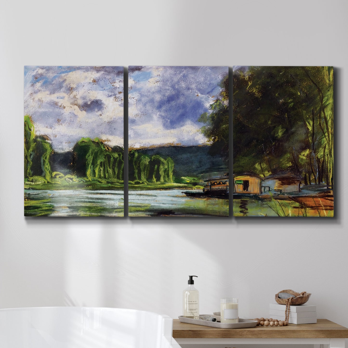 Three-panel canvas wall art featuring riverbank landscape near village, displayed in a bathroom above a bathtub.
