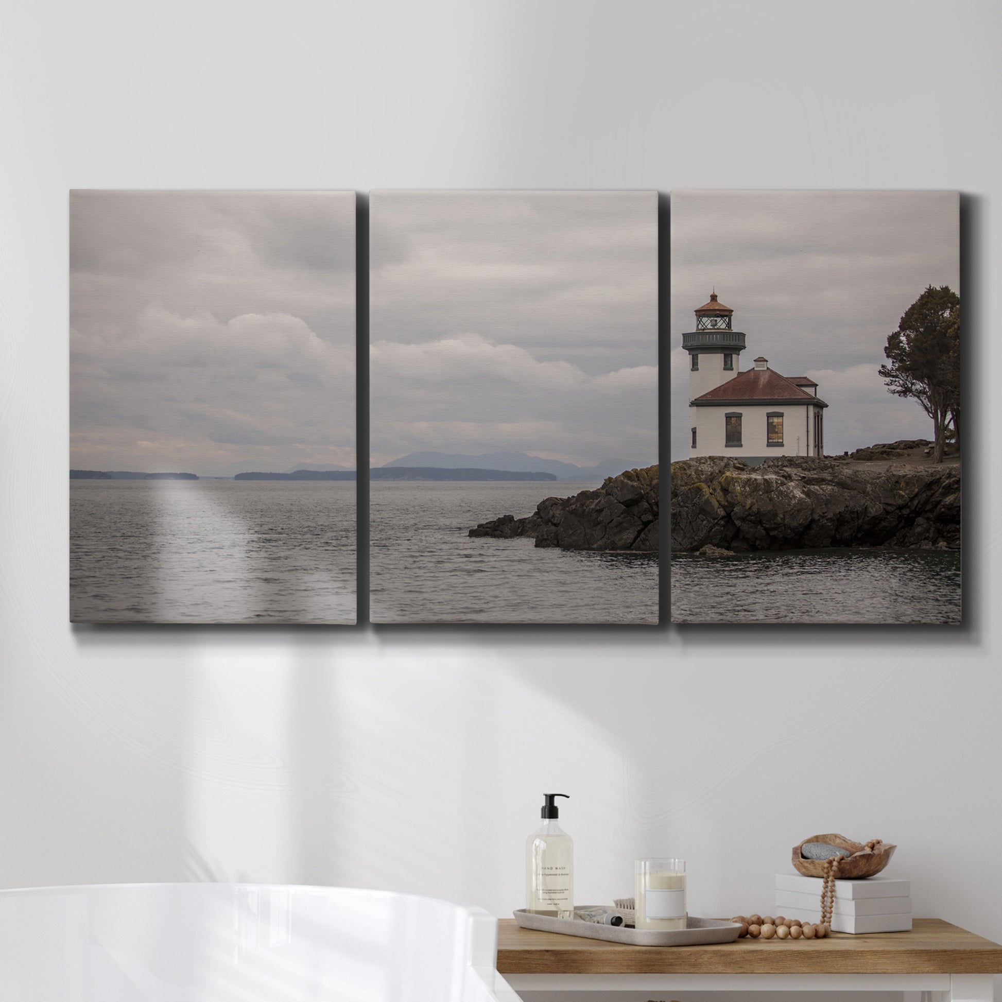 Three-panel canvas wall art featuring lighthouse watching over coastline, displayed in a bathroom above a bathtub.