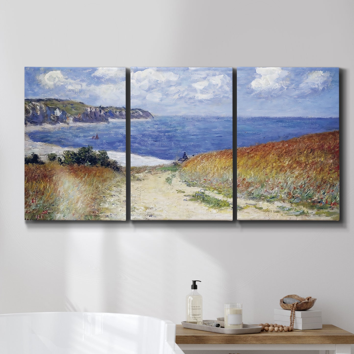 Three-panel canvas wall art featuring coastal path leading to sea, displayed in a bathroom above a bathtub.