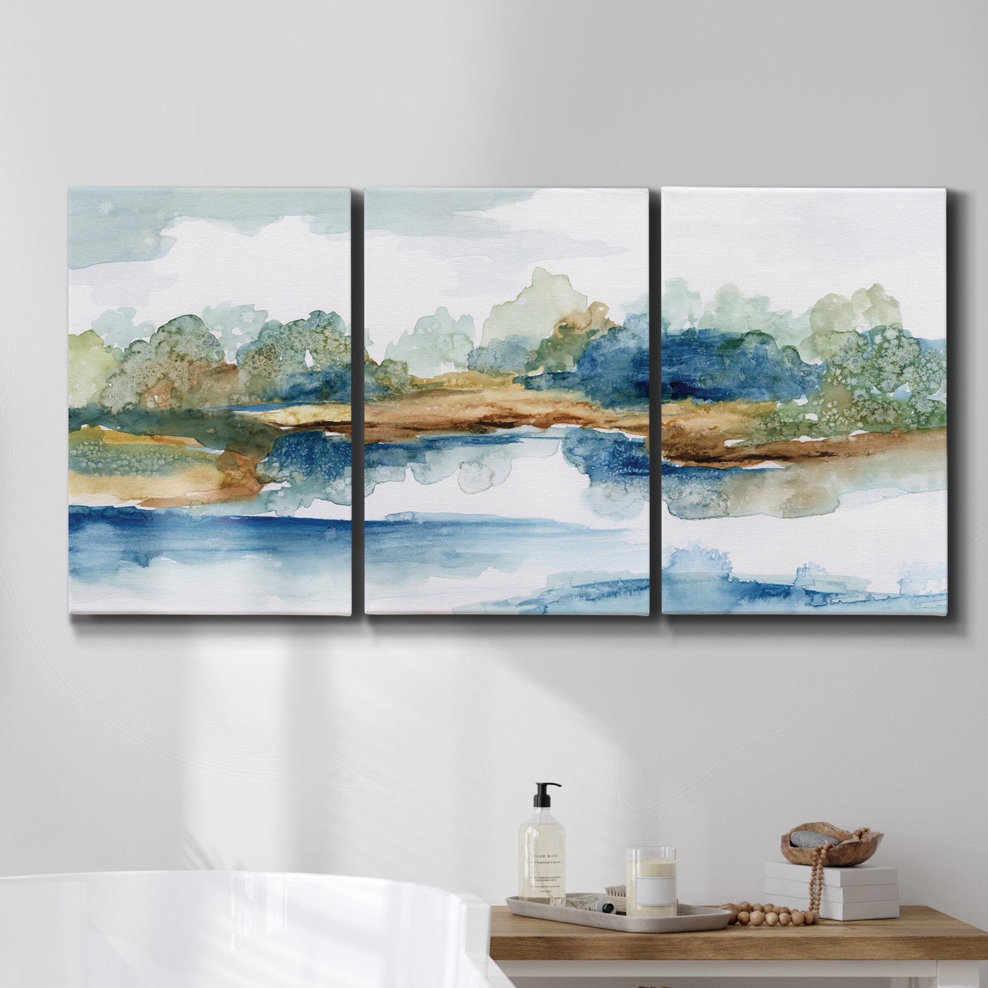 Three-panel canvas wall art featuring abstract blue watercolor landscape, displayed in a bathroom above a bathtub.