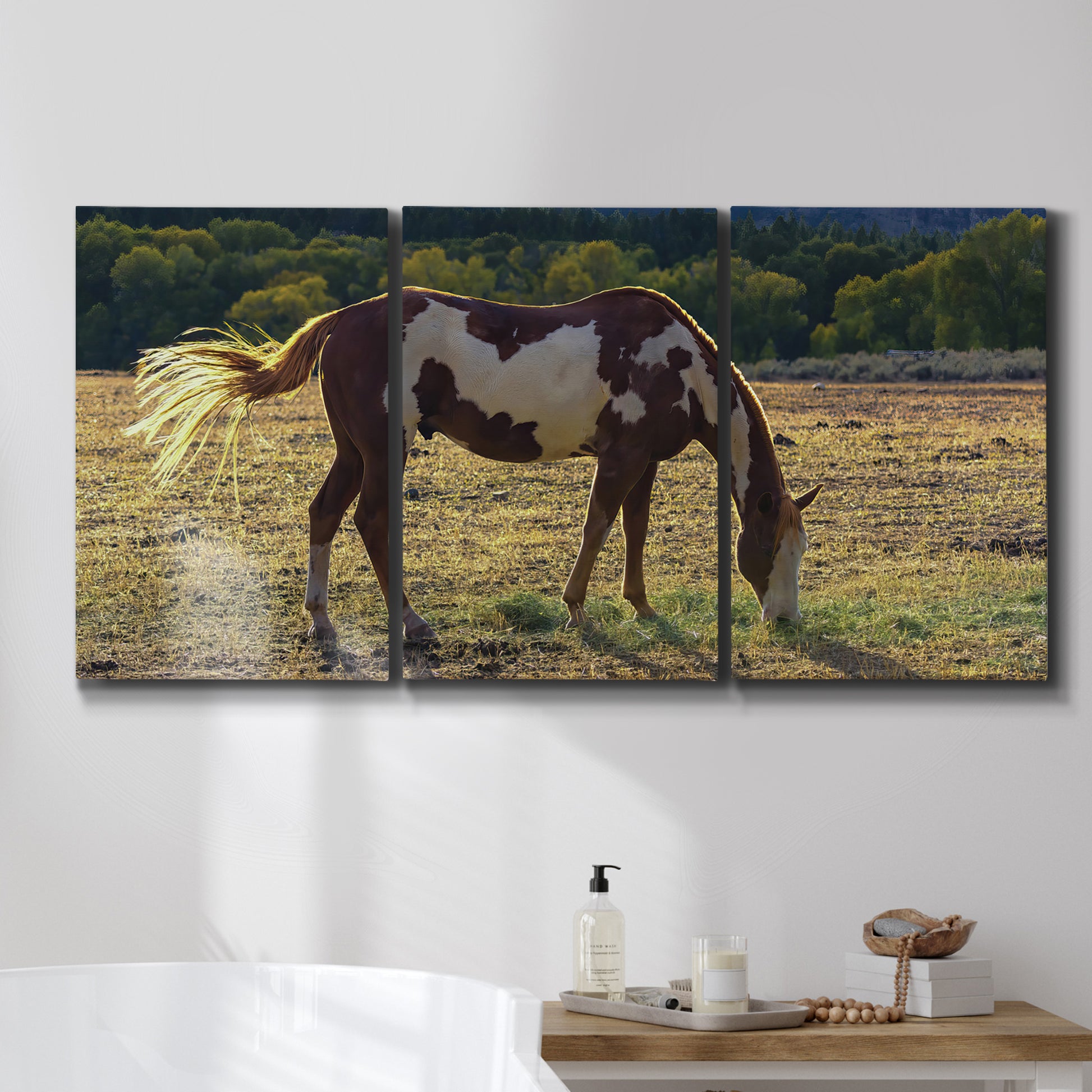 Three-panel canvas wall art featuring horses standing near farmhouse, displayed in a bathroom above a bathtub.