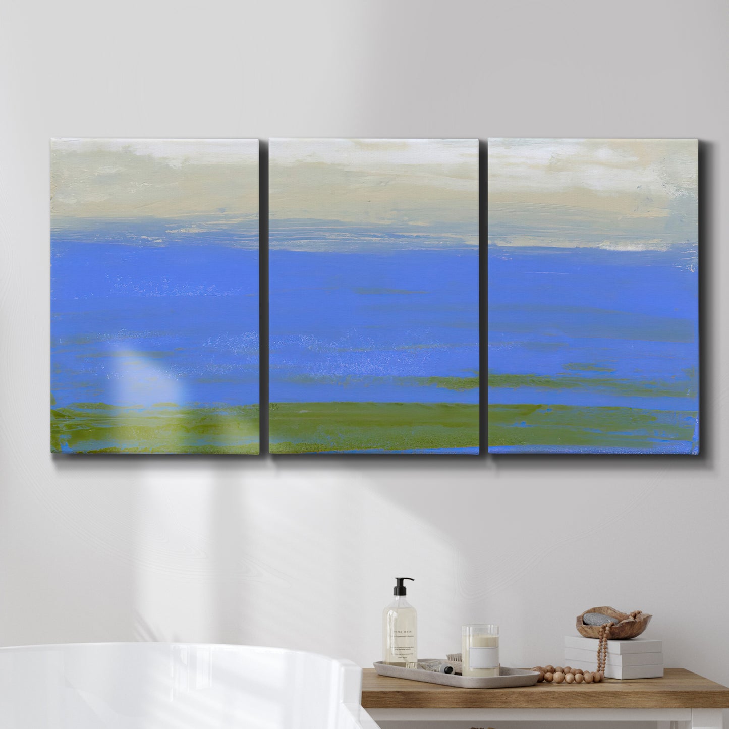 Three-panel canvas wall art featuring abstract coastal inlet landscape, displayed in a bathroom above a bathtub.