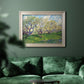 Impressionist spring orchard landscape by Vincent van Gogh in an ornate champagne frame displayed in a dark-toned interior setting.