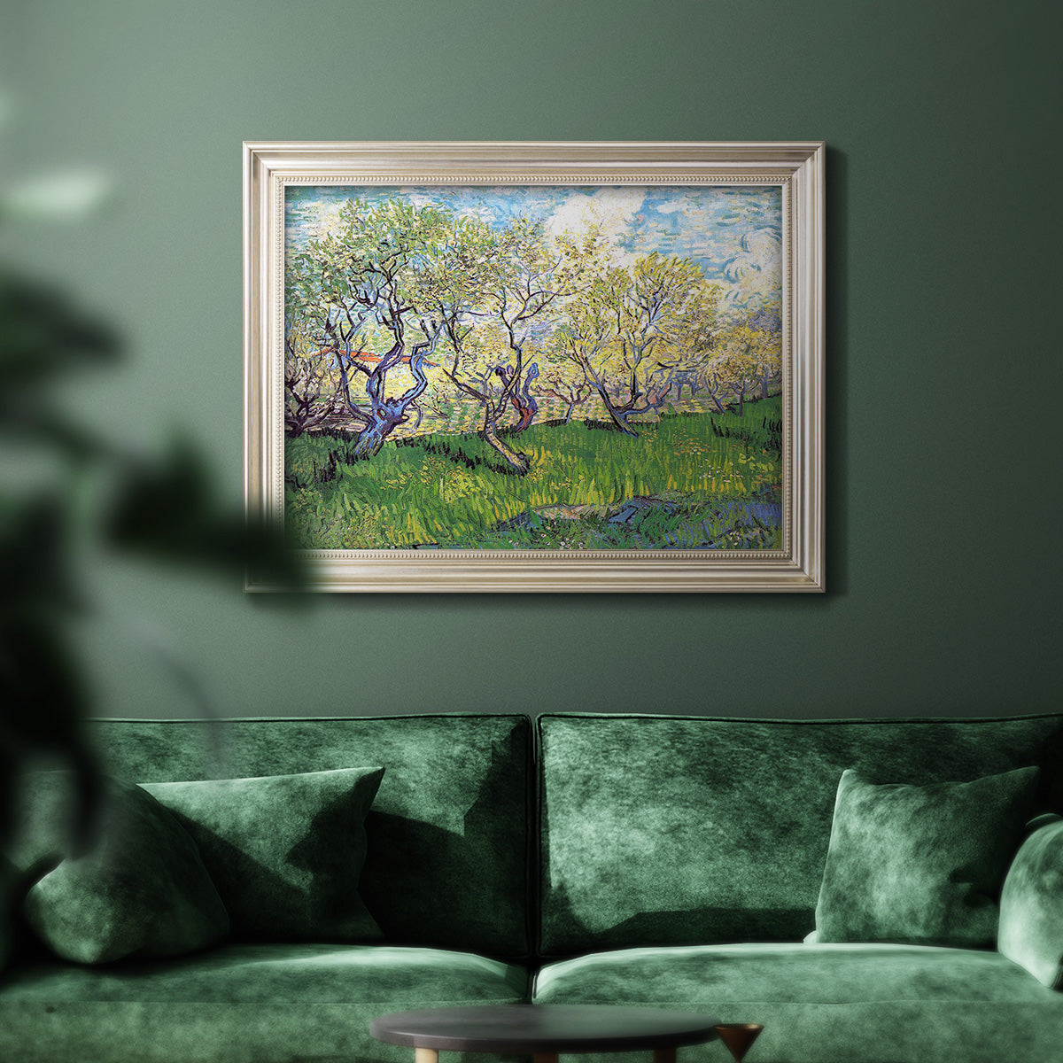 Impressionist spring orchard landscape by Vincent van Gogh in an ornate champagne frame displayed in a dark-toned interior setting.