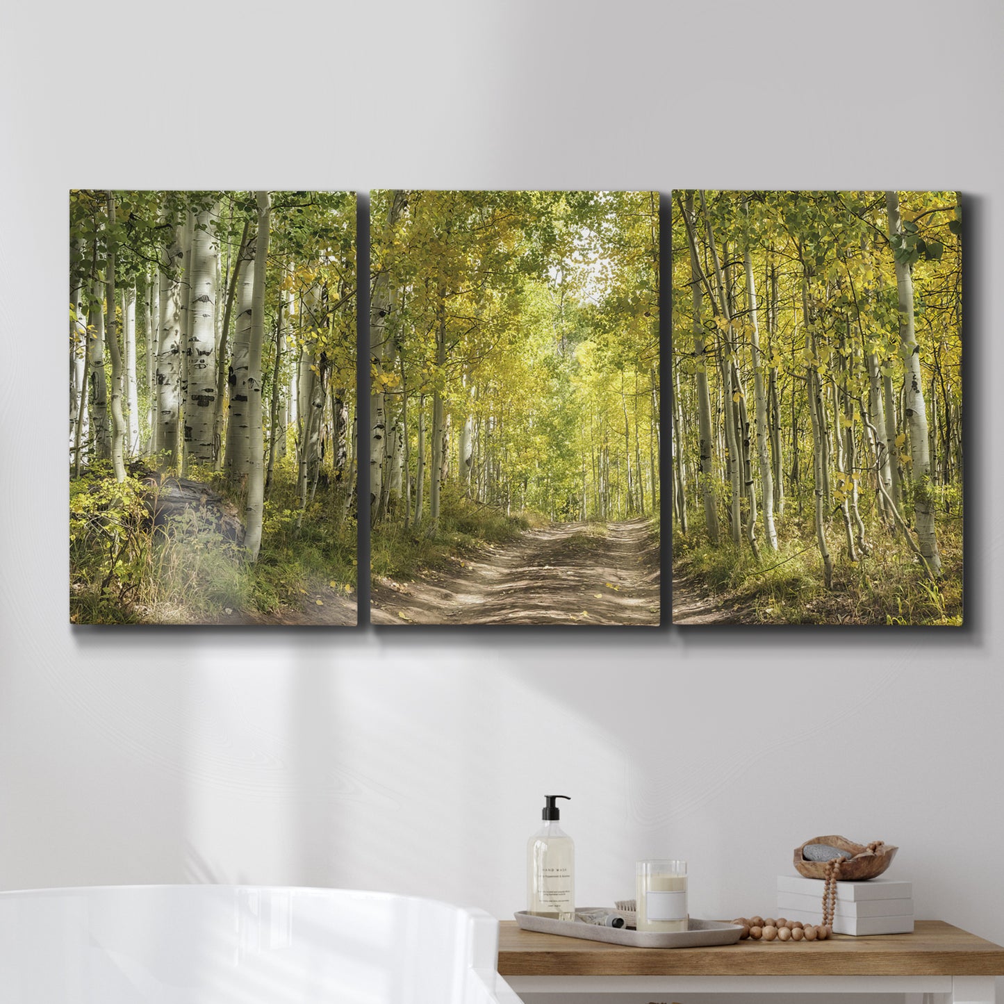 Three-panel canvas wall art featuring tree lined forest road photograph, displayed in a bathroom above a bathtub.
