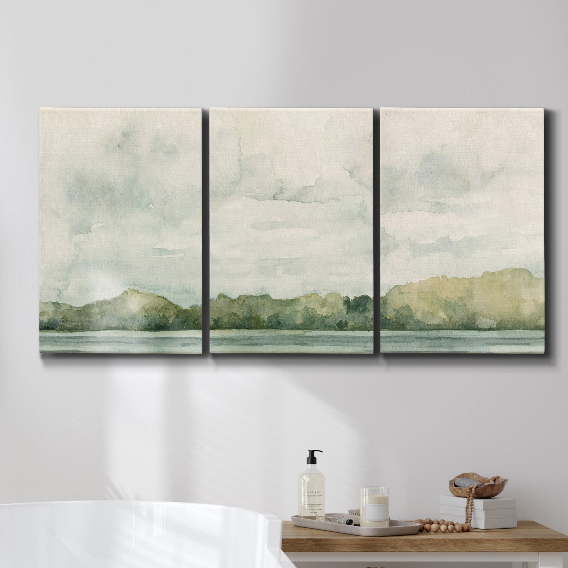 Three-panel canvas wall art featuring riverbank landscape with trees, displayed in a bathroom above a bathtub.